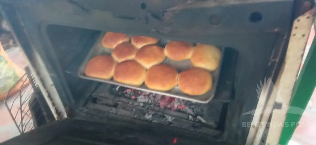 Belizean coconut-raisin buns in a wood-fired oven made from a converted stove, door open showing live coals beneath the baking tray