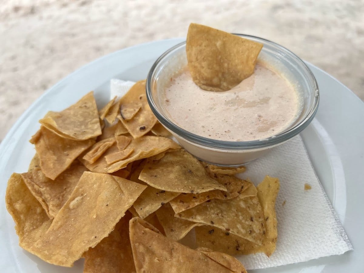 Belizean cheese dip with a tortilla chip dipped in, served on a plate by the beach in Belize
