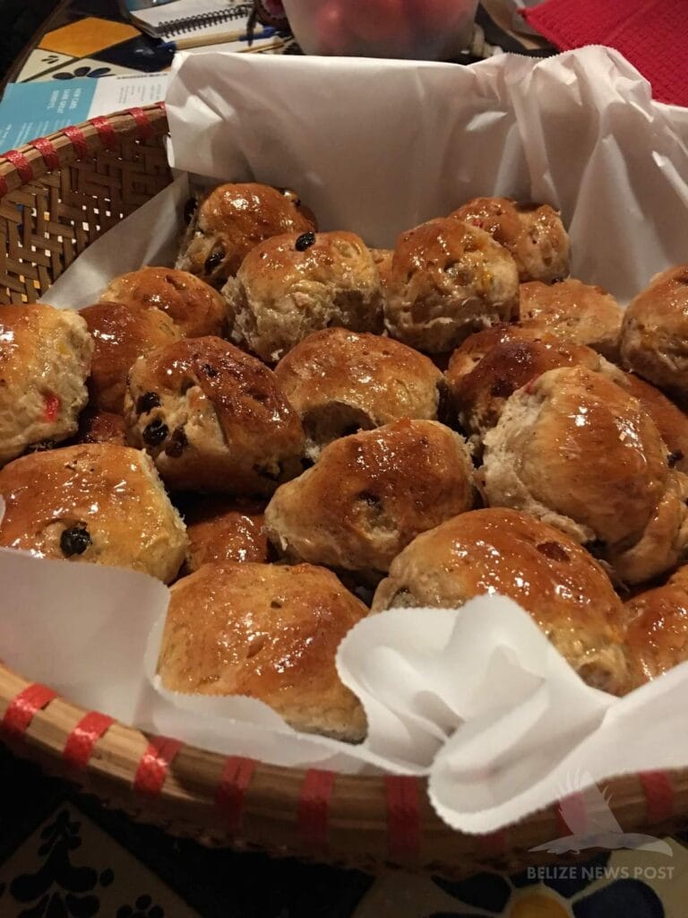 Belizean Creole coconut-raisin buns in a paper-lined woven basket, glazed golden brown with raisins throughout