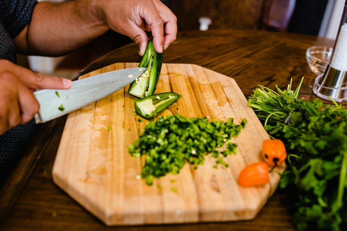 Hands chopping a jalapeño on a wooden cutting board with diced cilantro and a habanero pepper for Belizean cheese dip