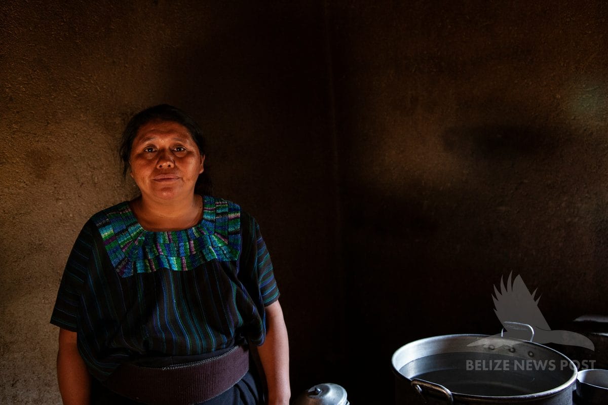 Maya woman in traditional dress standing in adobe kitchen with cooking pots — chulibuul, Belize