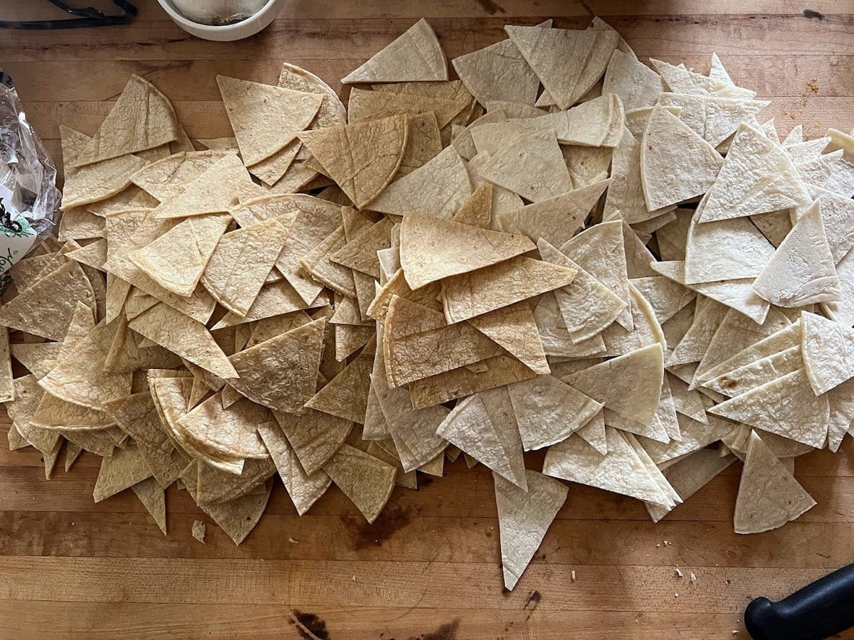 Hand-cut corn tortilla triangles spread out on a surface to dry before frying for Belizean cheese dip