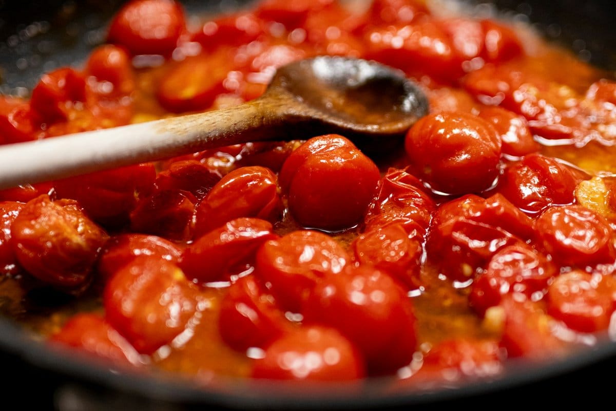 Fresh tomatoes cooking down in a pan with a wooden spoon to make the tomato sauce base for Belizean cheese dip