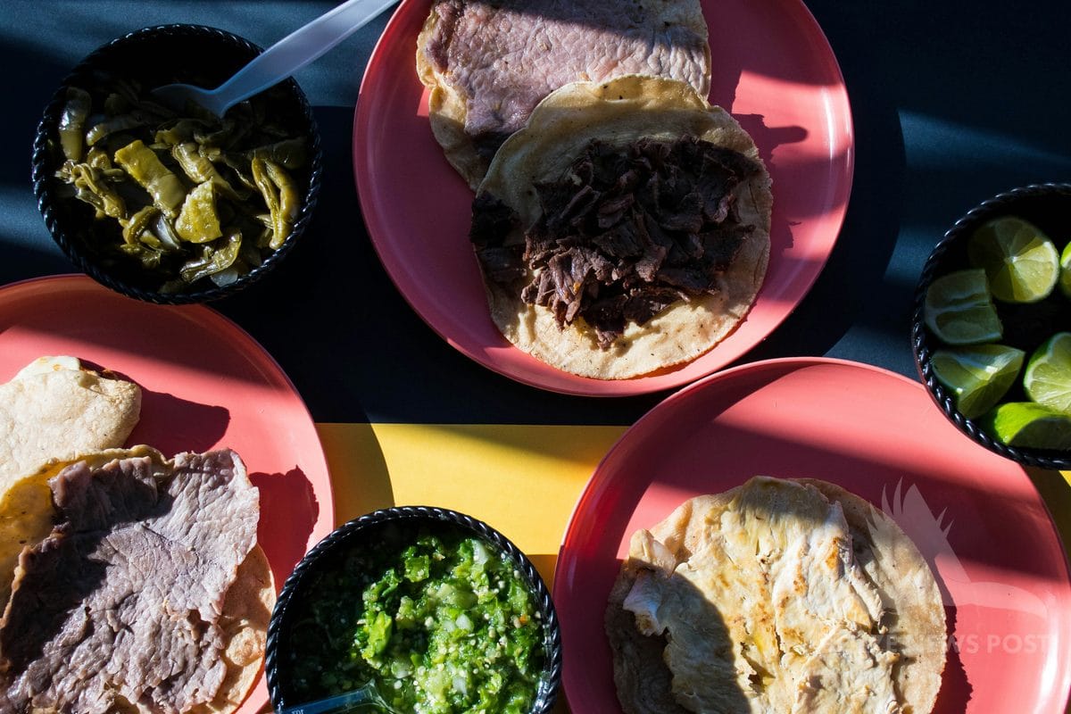 Poc chuc spread — grilled pork on corn tortillas with pickled chiles, green salsa, and lime wedges on red plates