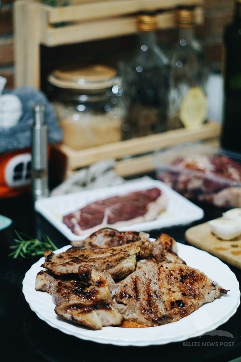 Poc chuc grilled pork on a white plate with raw pork loin in background ready to marinate, Belize