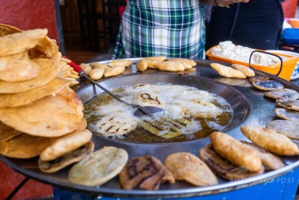 Polcanes frying in oil in a large pan, with white cheese and tostadas at a street food stall