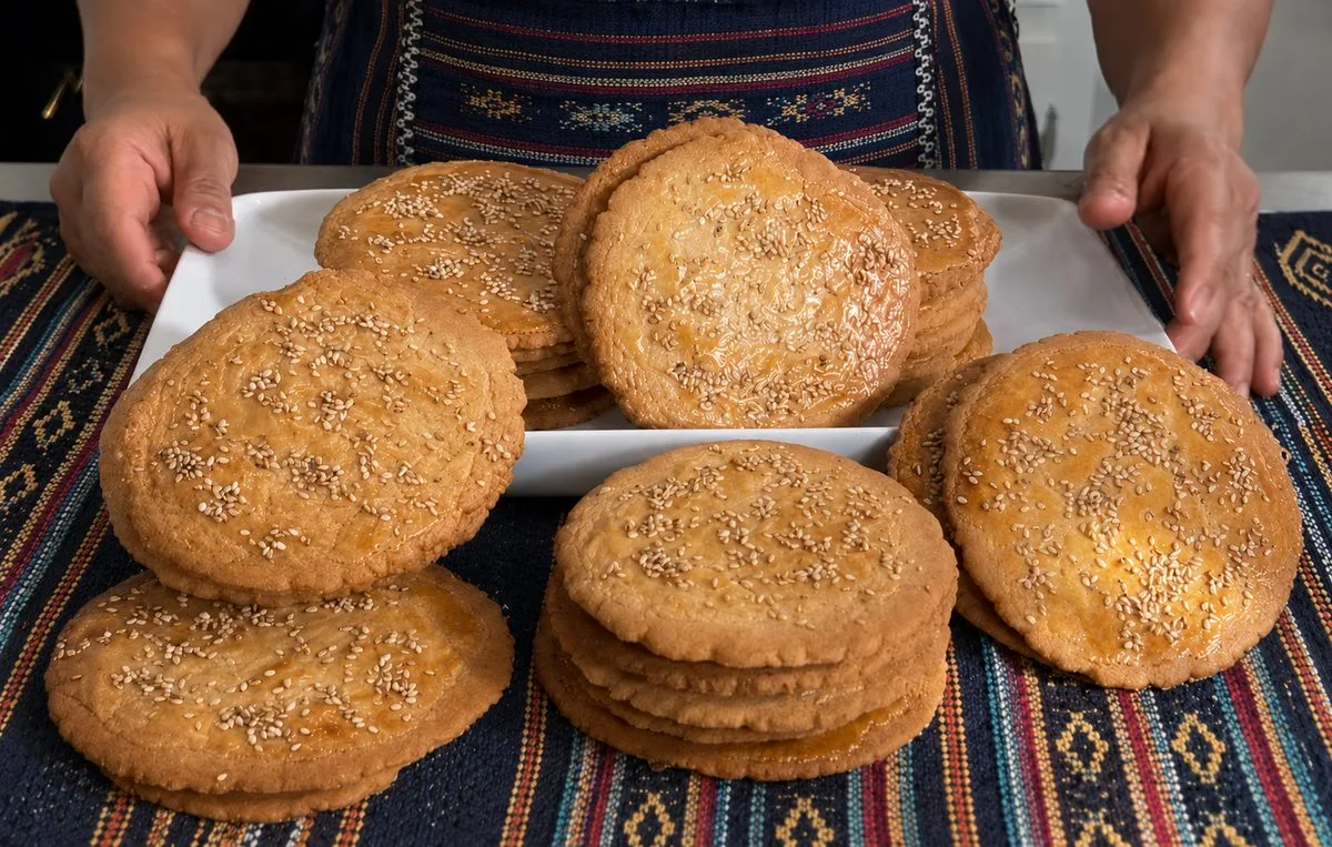 Stacks of Belizean champurradas, flat sesame-topped cookies, on a white platter over a striped woven cloth