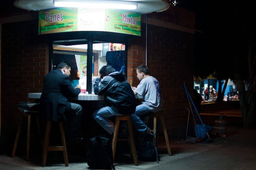 Guatemalan shuco street cart at night, menu listing longaniza chorizo carne salchicha