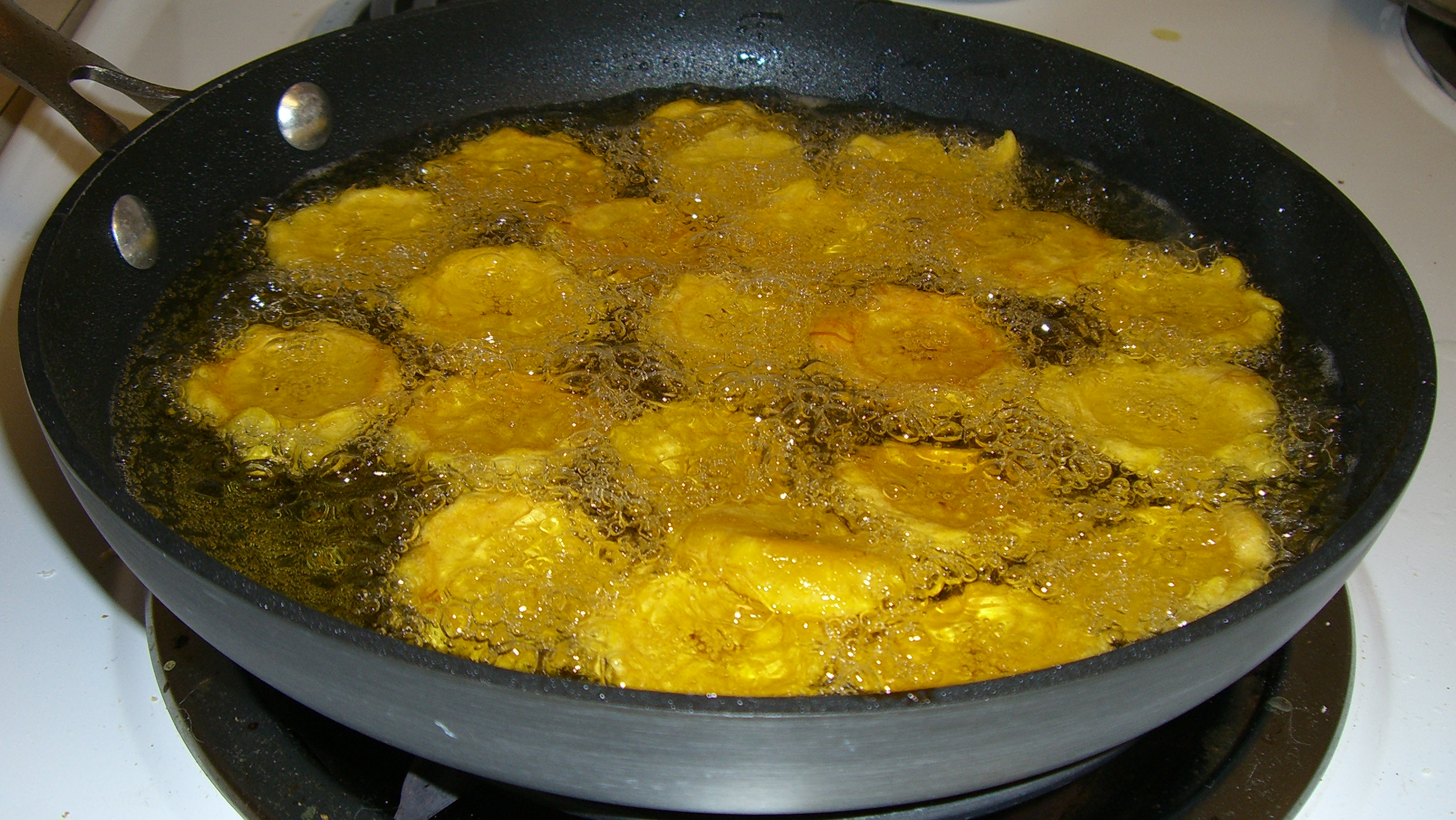 Plantains frying in oil in a heavy pan, showing the golden color that indicates proper cooking for empanadas de platano