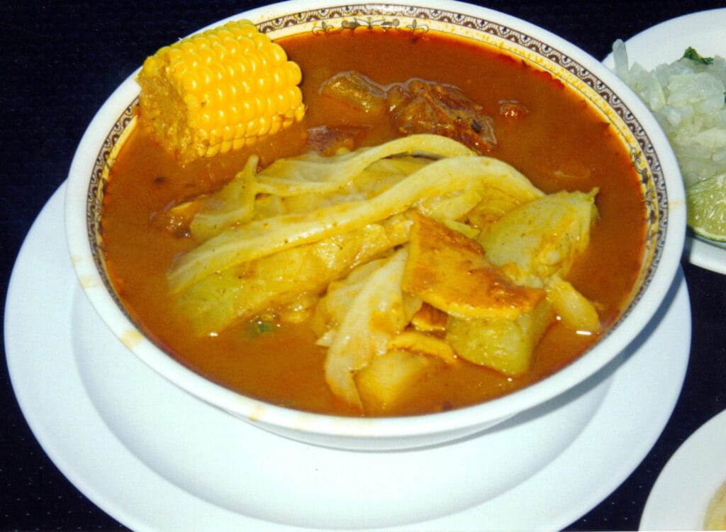 Bowl of sopa de pata with cow feet, yuca, corn, and vegetables in achiote broth