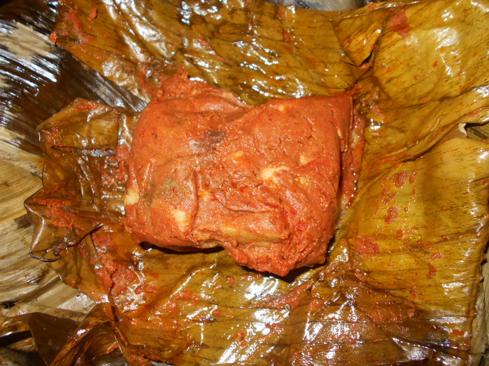 Guatemalan tamal colorado opened from its banana leaf showing red recado masa with olive and pepper