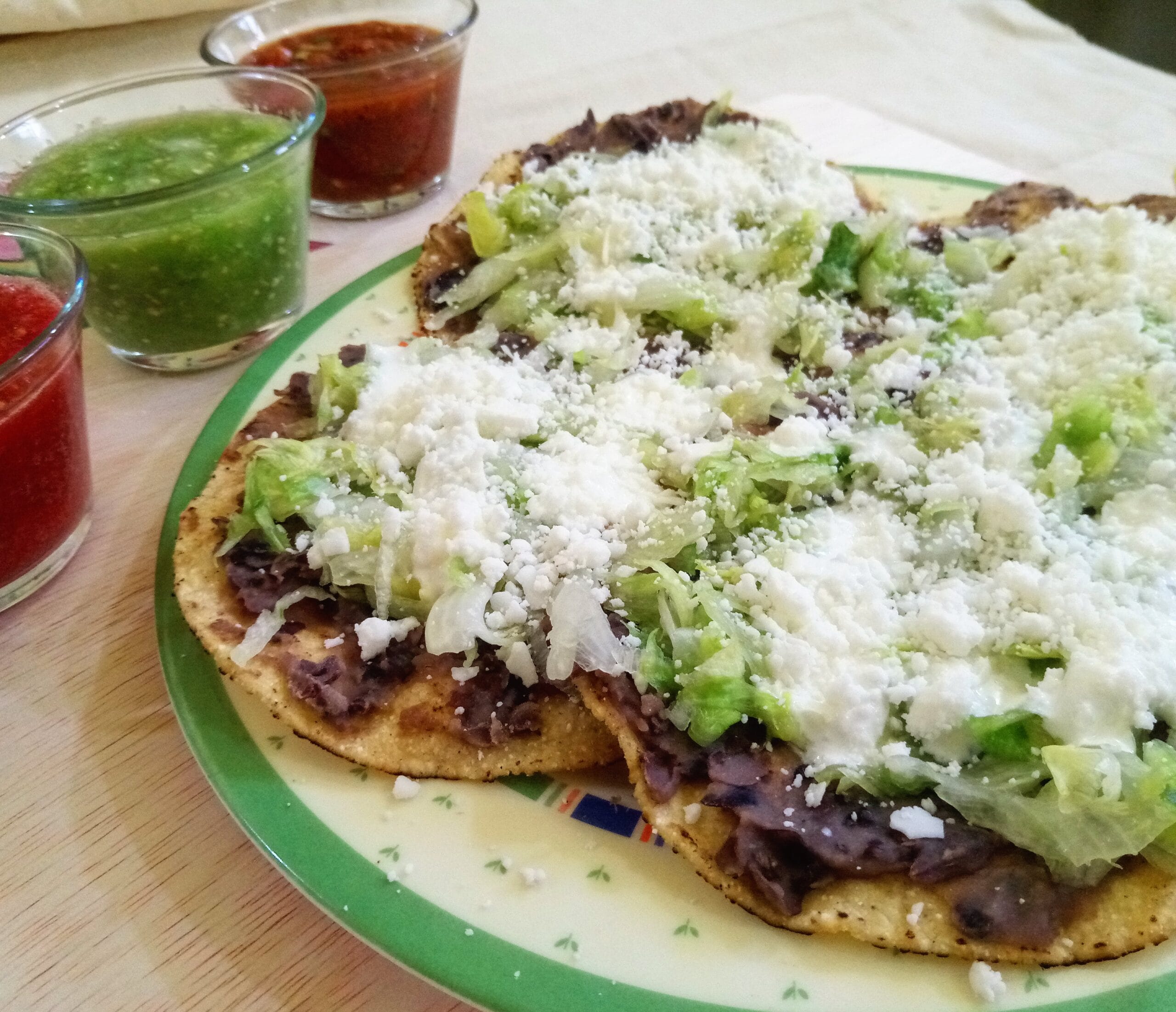 Crisp fried corn tortillas topped with refried beans and grated dry cheese, the same beans-and-cheese build as catrachas
