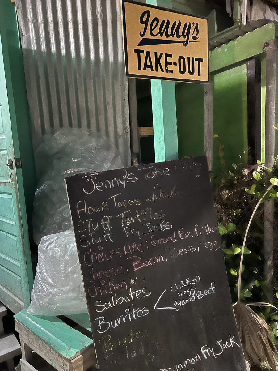 A Belizean street food stand at night with a chalkboard menu of tacos, salbutes and panades