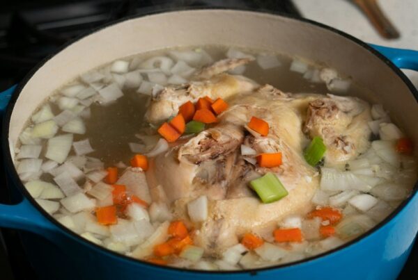 A whole chicken simmering with vegetables for a caldo