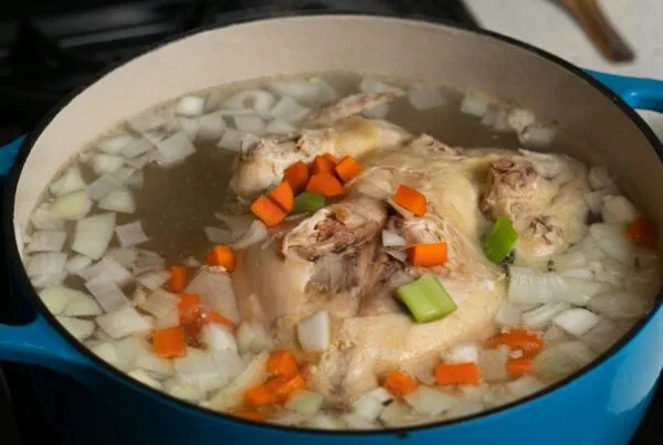 A whole chicken simmering with vegetables for a caldo