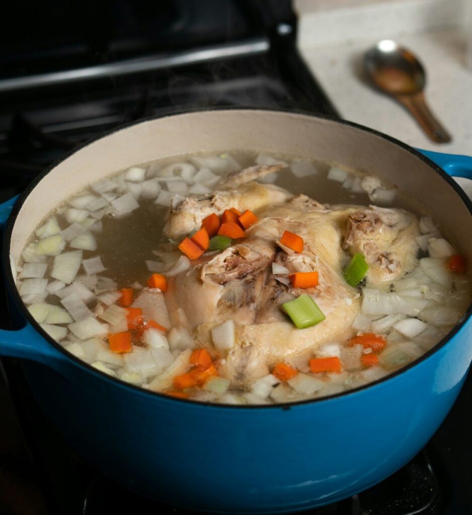 A whole chicken simmering with vegetables for a caldo