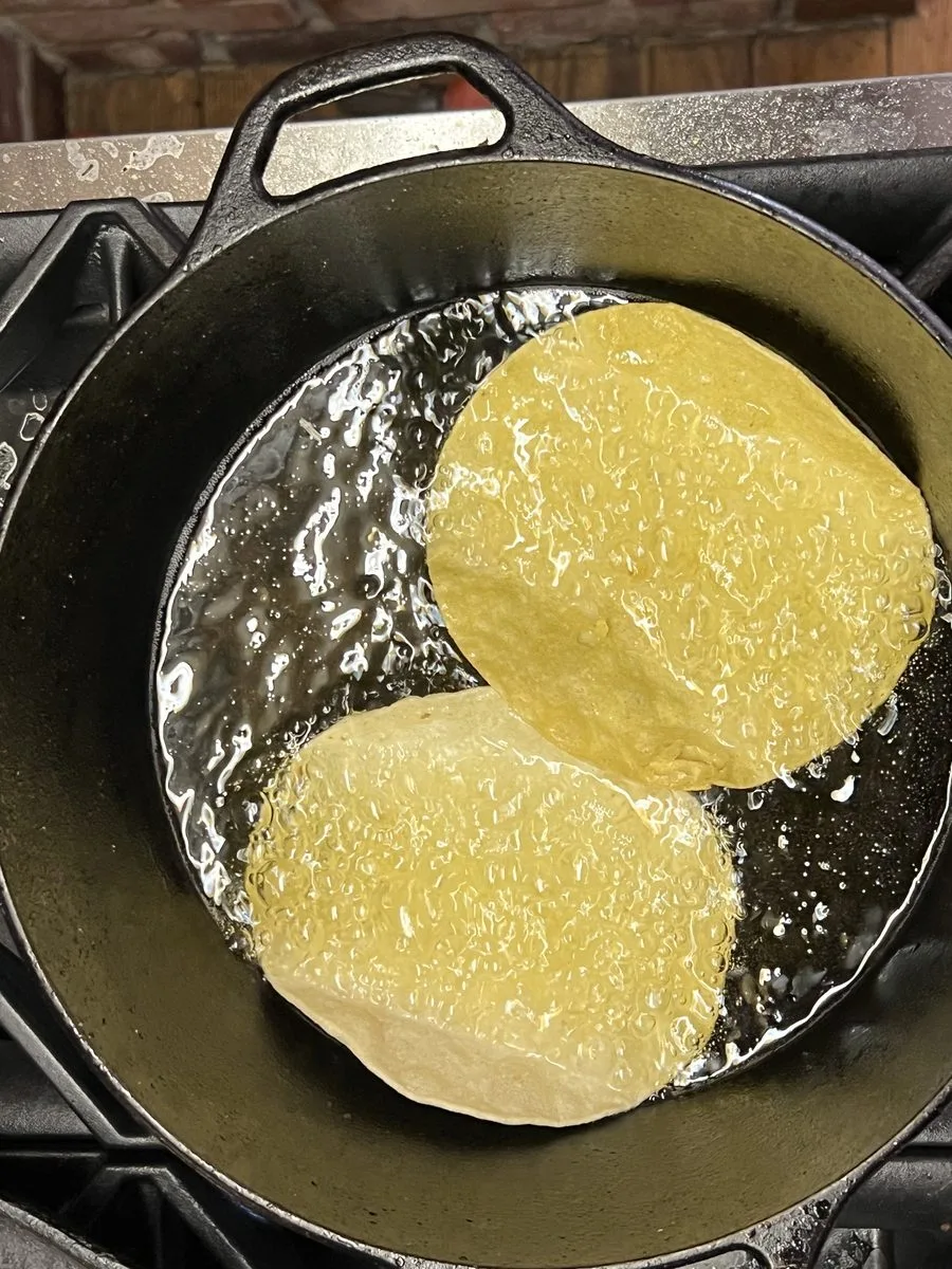 Corn tortillas frying in oil in a cast-iron pan to make catrachas
