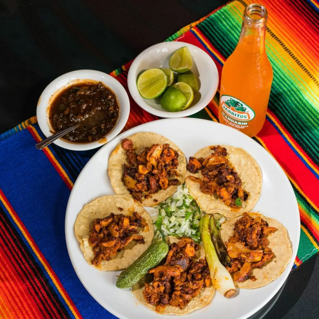 A plate of corn-tortilla tacos with lime, salsa, and onion