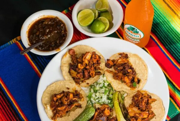 A plate of corn-tortilla tacos with lime, salsa, and onion