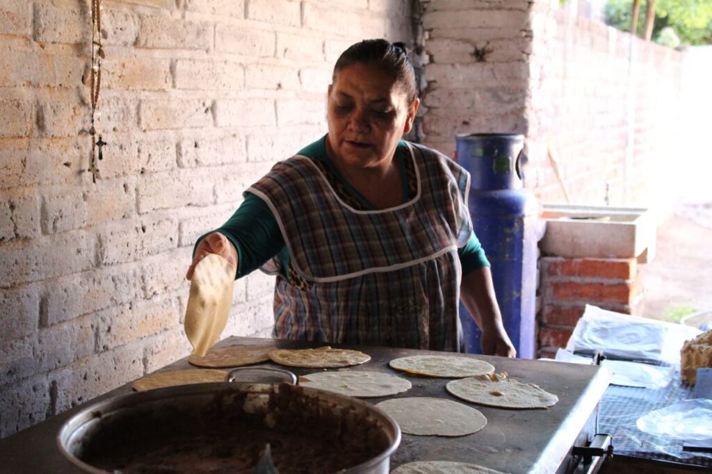 Honduran woman shaping fresh corn tortillas on a comal in a rustic kitchen