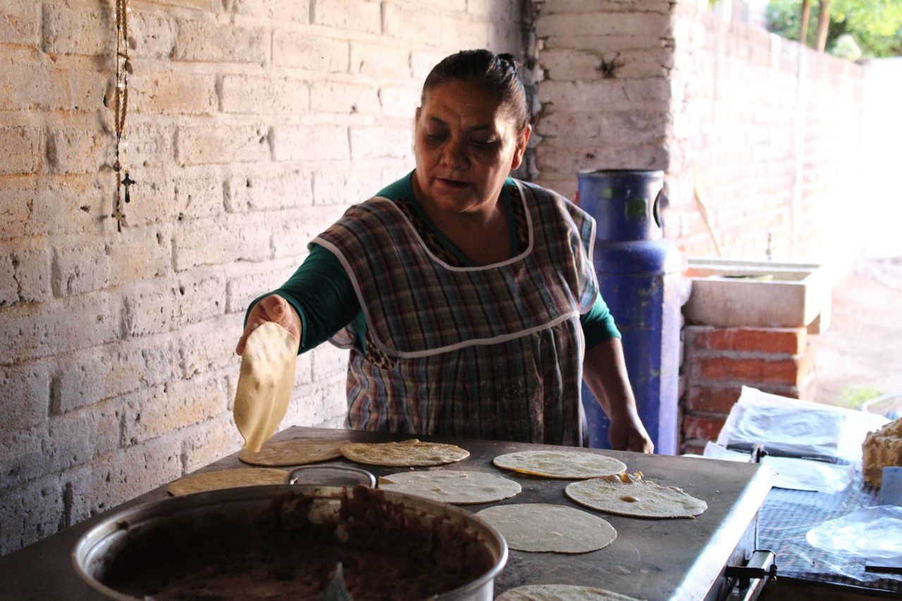 Honduran woman shaping fresh corn tortillas on a comal in a rustic kitchen