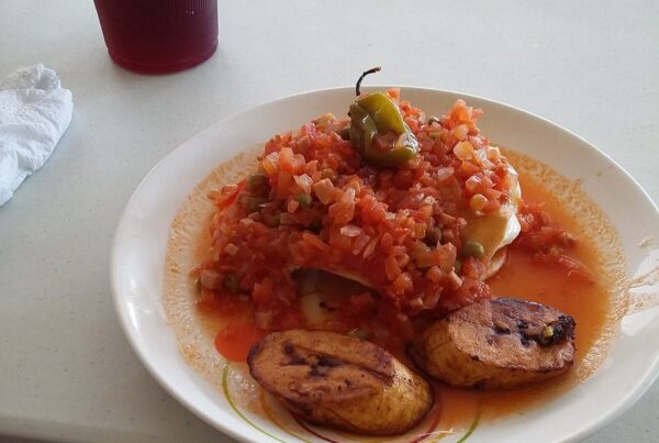 A plate of huevos motulenos with tomato sauce, fried plantain, and a chile