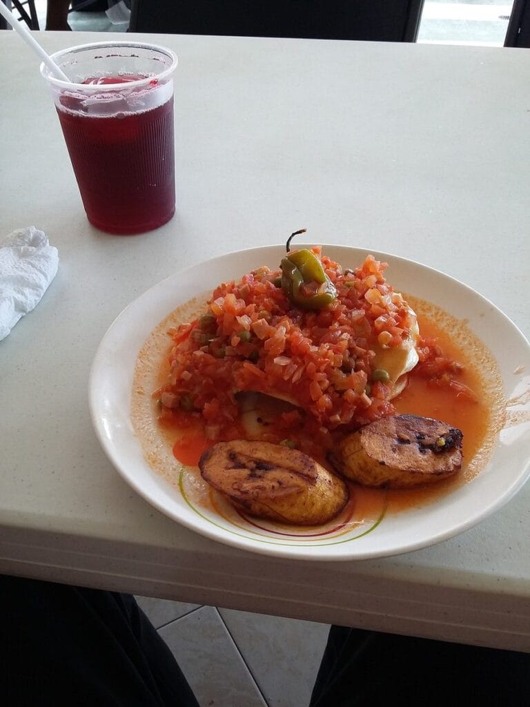 A plate of huevos motulenos with tomato sauce, fried plantain, and a chile