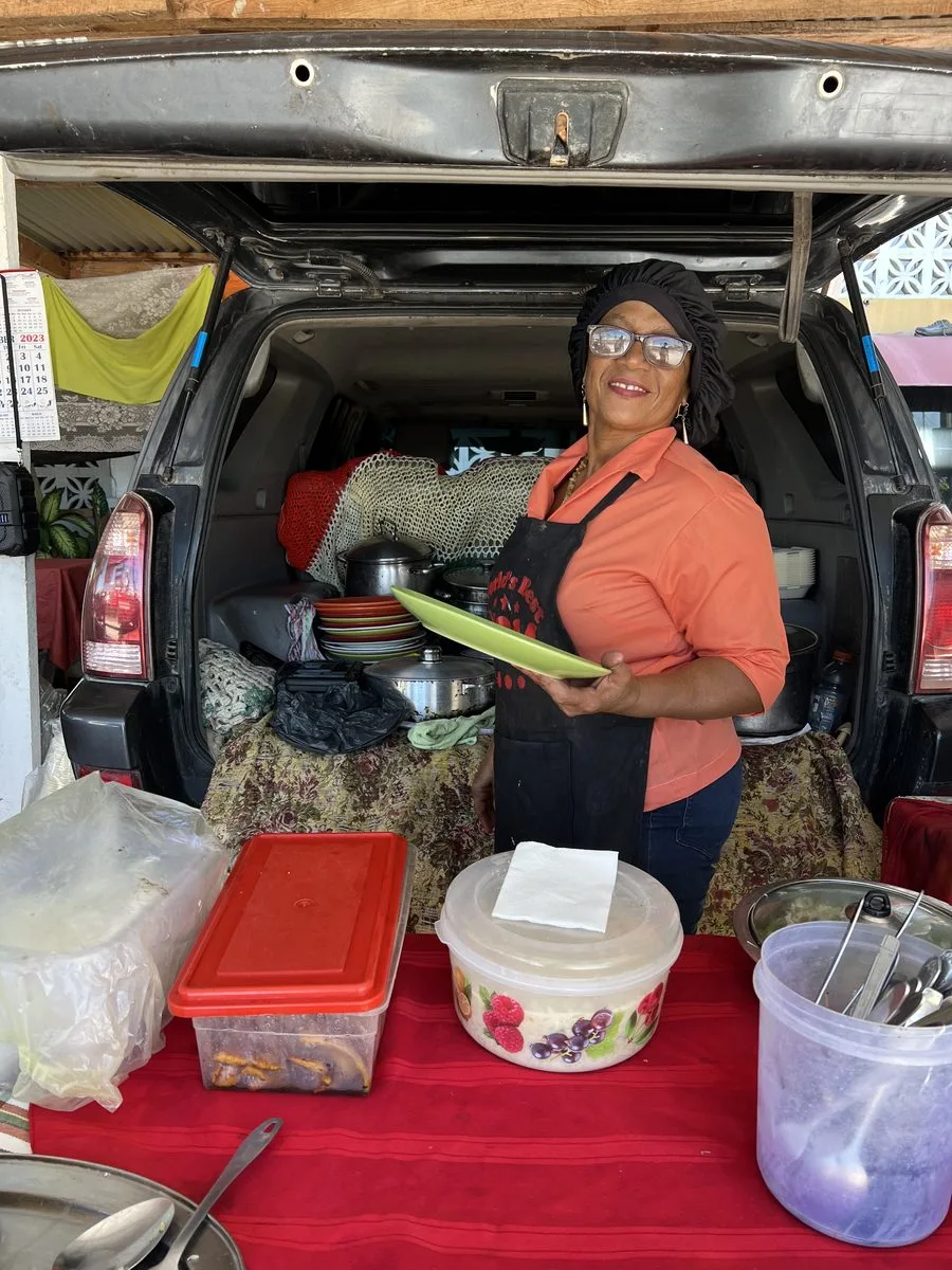 Margaret Hendy of Margaret's Fireheart Food smiling with a plate at her stand across from Belize's Philip Goldson airport