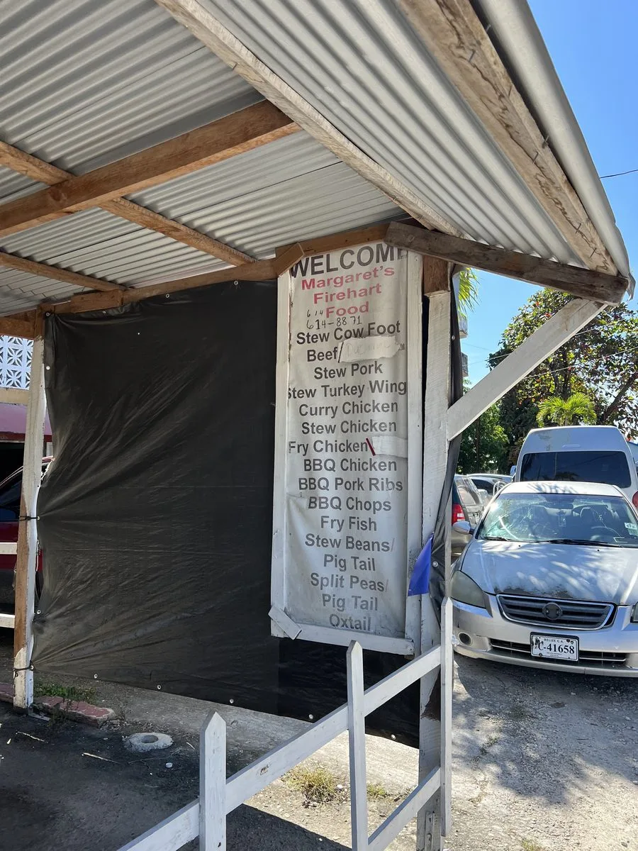Margaret's Fireheart Food menu board listing stew cow foot, oxtail, pigtail and barbecue near the Belize airport