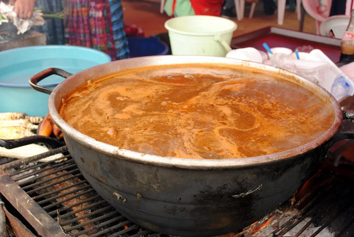Bowl of Guatemalan pepián de pollo, chicken in a dark toasted-seed recado with vegetables