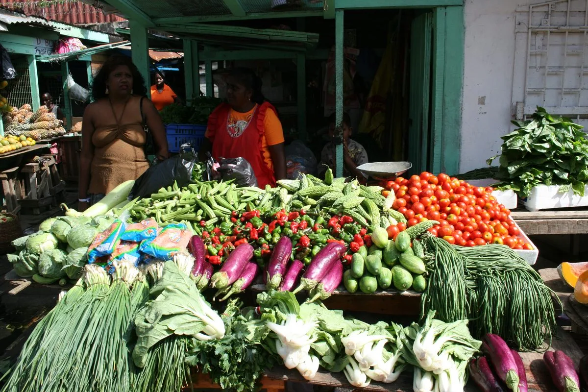 Purple eggplants, cabbage, tomatoes, and greens at a Caribbean produce market, ingredients used in Haitian legim