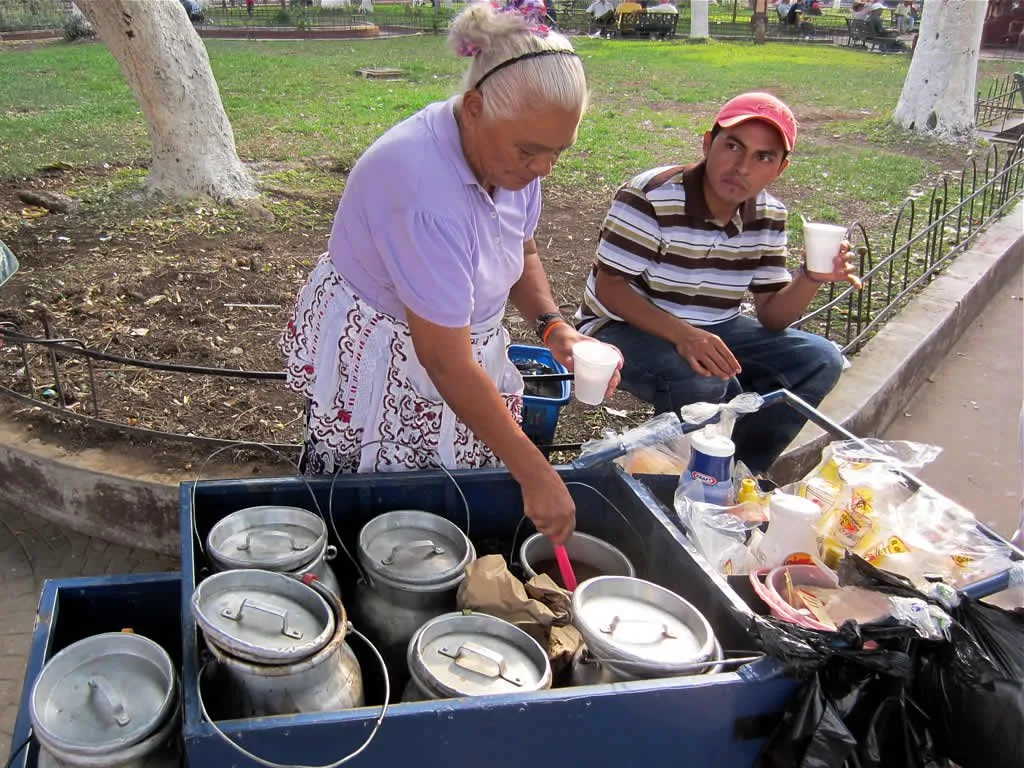 A Salvadoran street vendor serves hot atoles from aluminum pots