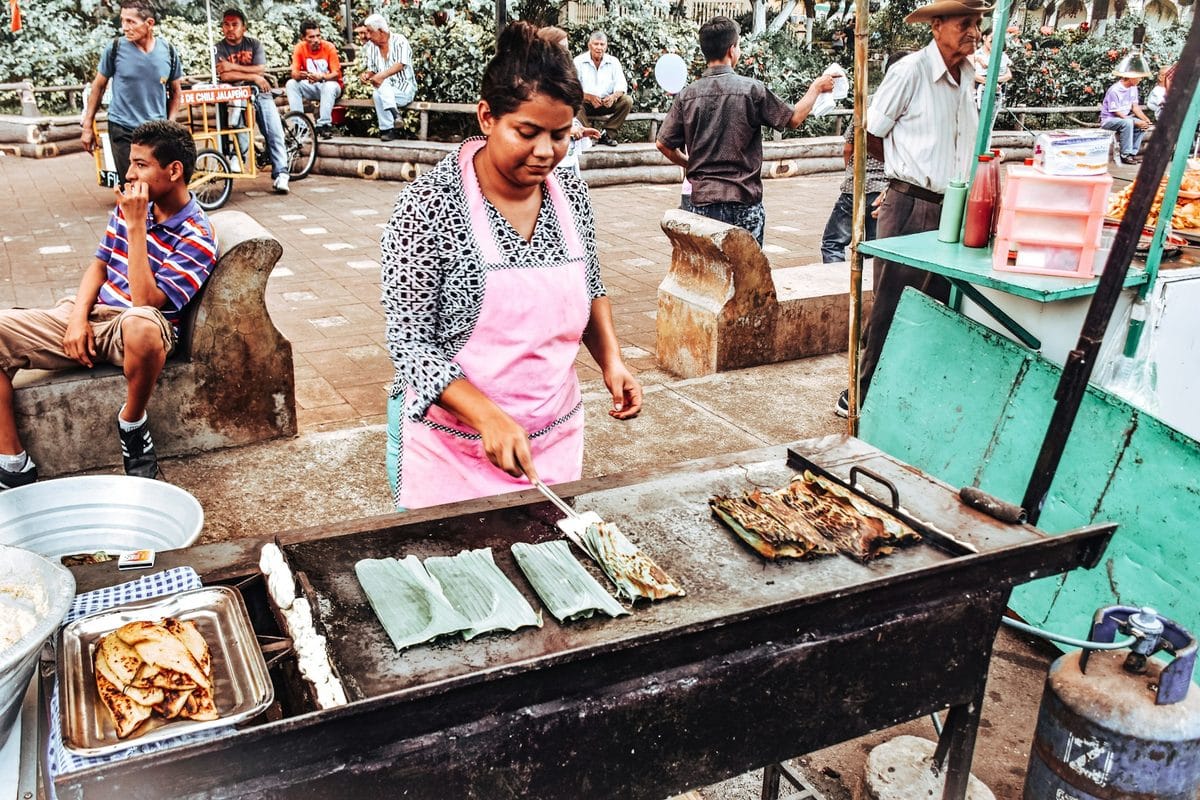 A Salvadoran street vendor griddles banana-leaf-wrapped corn cakes on a comal, the method behind riguas