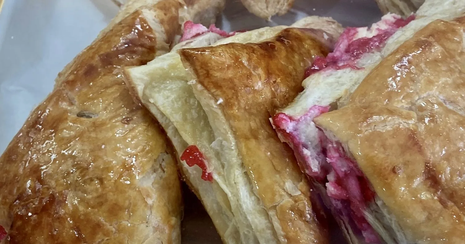 Triangular guava and cheese pastelitos, glazed and stacked in a Cuban bakery case