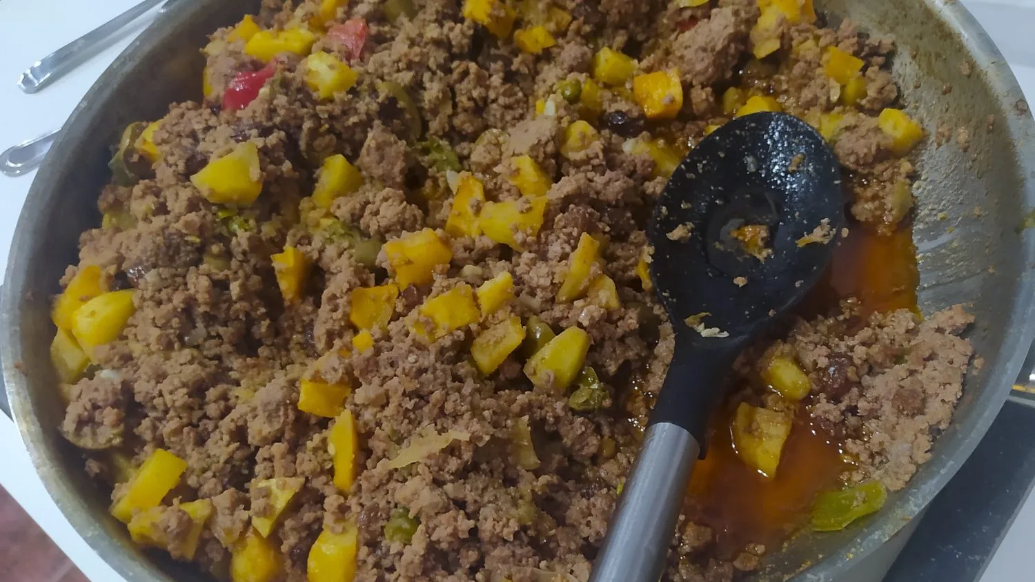 Cuban picadillo with diced potato, green olives and sweet peppers cooking in a wide skillet