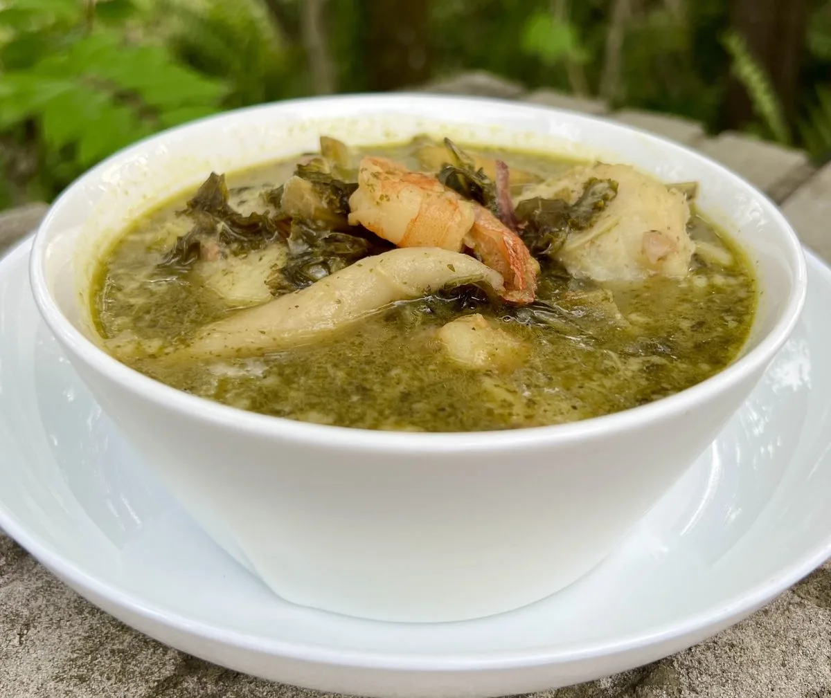 Jamaican pepperpot soup, a thick green callaloo soup with spinners, served in a white bowl