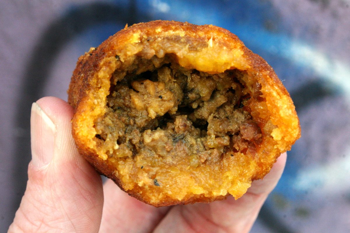 an alcapurria broken open to show the orange green-banana masa around a seasoned ground beef filling