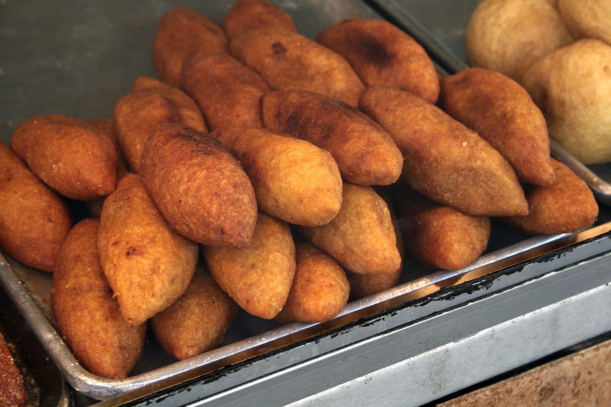 A kiosk tray piled with fried Puerto Rican alcapurrias, torpedo-shaped and deep golden