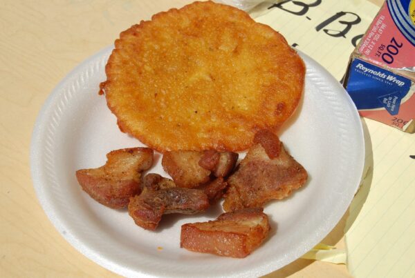A flat golden Puerto Rican bacalaito on a paper plate beside pieces of fried pork