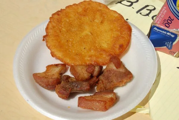 A flat golden Puerto Rican bacalaito on a paper plate beside pieces of fried pork