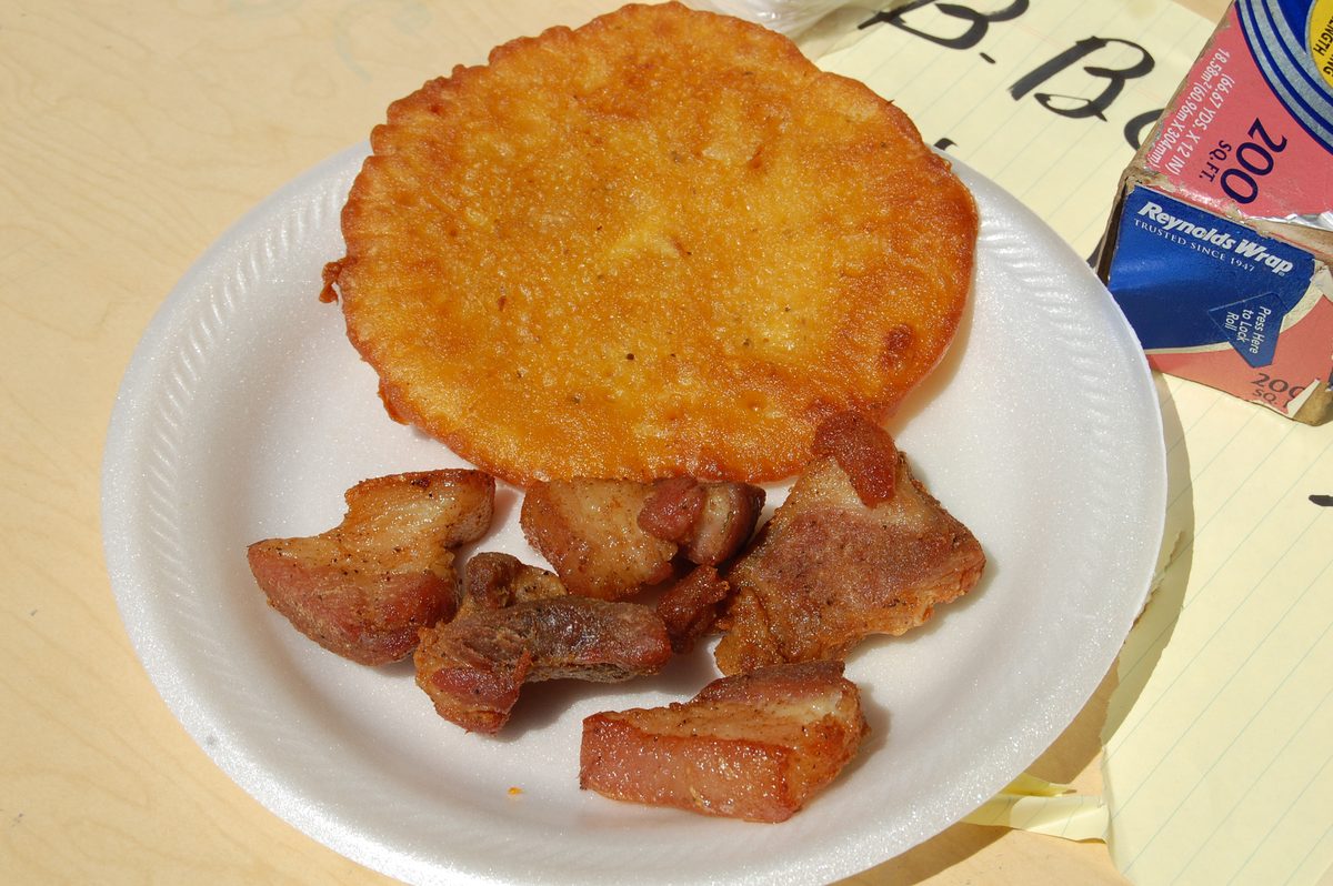 A flat golden Puerto Rican bacalaito on a paper plate beside pieces of fried pork