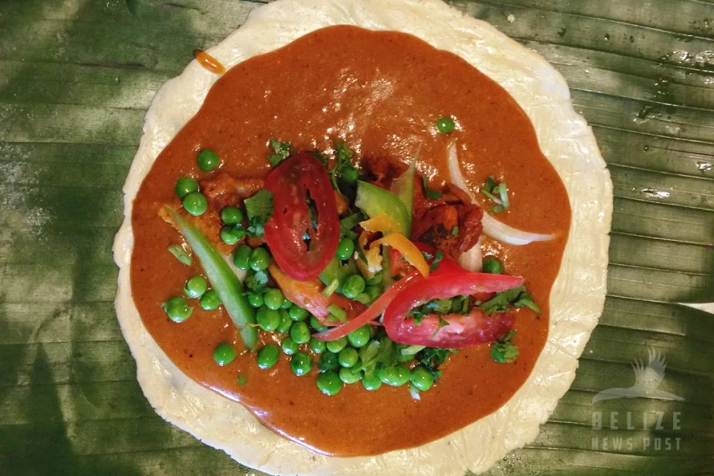 A Belizean tamale opened on its plantain leaf showing the masa, meat and cull gravy